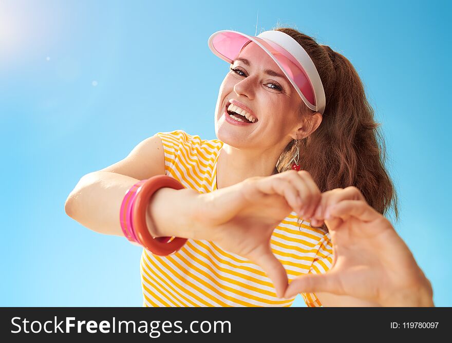 Happy young woman in yellow shirt against blue sky showing heart shaped hands. Happy young woman in yellow shirt against blue sky showing heart shaped hands