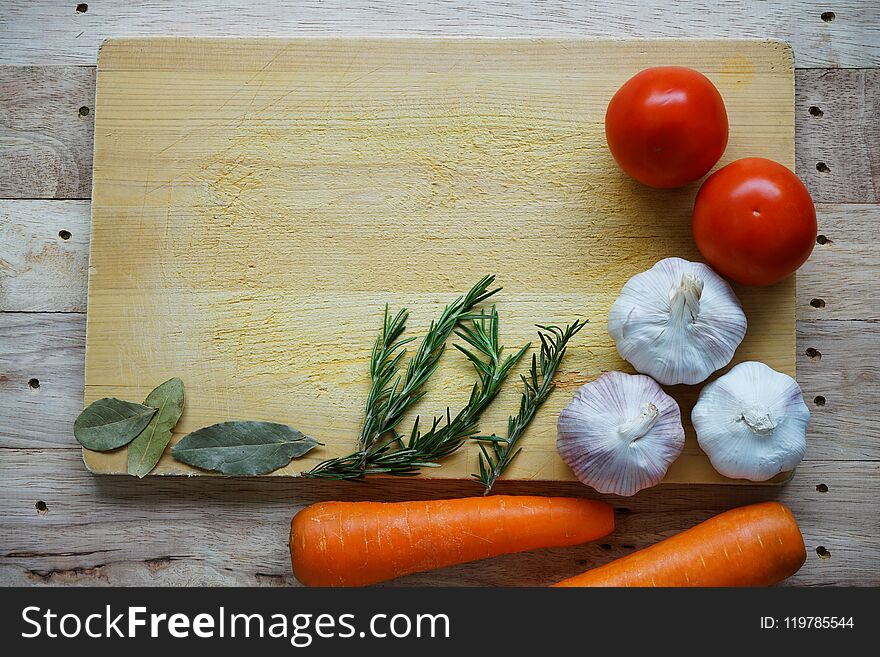 Many fresh ingredients, rosemary, spaghetti, carrot, tomato, garlic, onion and bay leaf on chopping board with wooden table background, copy space, cooking concept