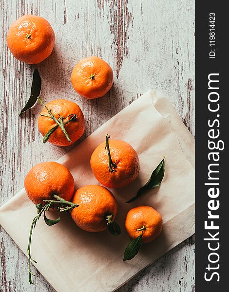 top view of tangerines with leaves on baking paper on rustic tabletop