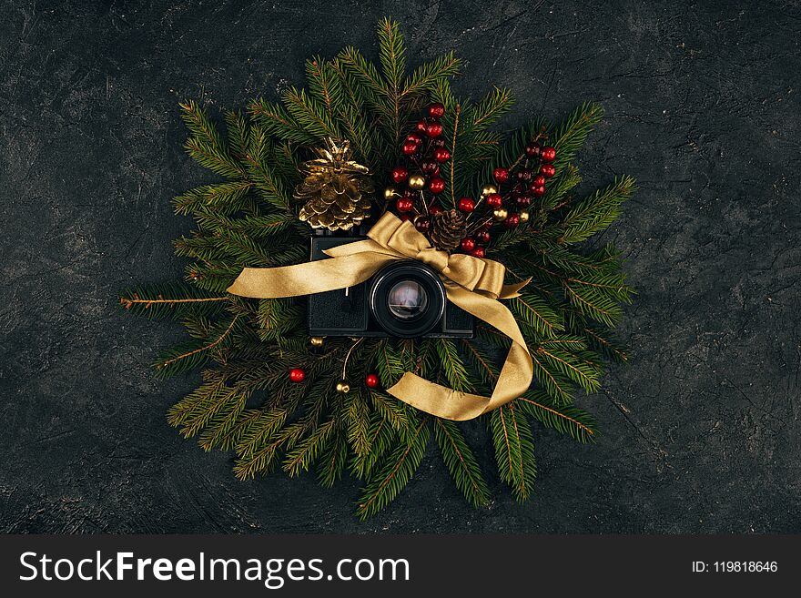 top view of photo camera and festive decorations on fir branches on dark tabletop