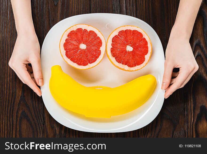 cropped shot of woman holding plate with halved grapefruit and banana case