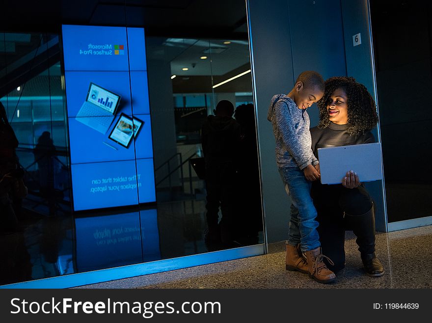 Boy in Gray Hoodie Standing Beside Woman Holding Laptop