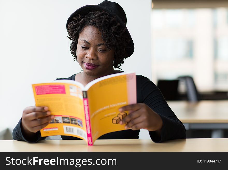 Woman in Black Long-sleeved Shirt Reading a Yellow Covered Book