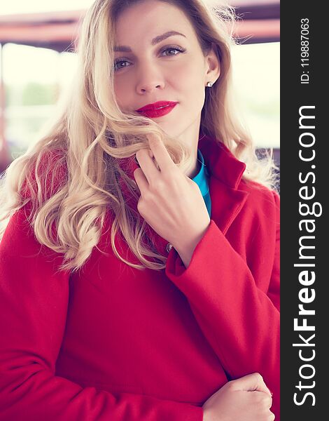 Outdoor fashion portrait of glamour young cheerful stylish lady wearing trendy red coat. Blonde long hair. Style photo