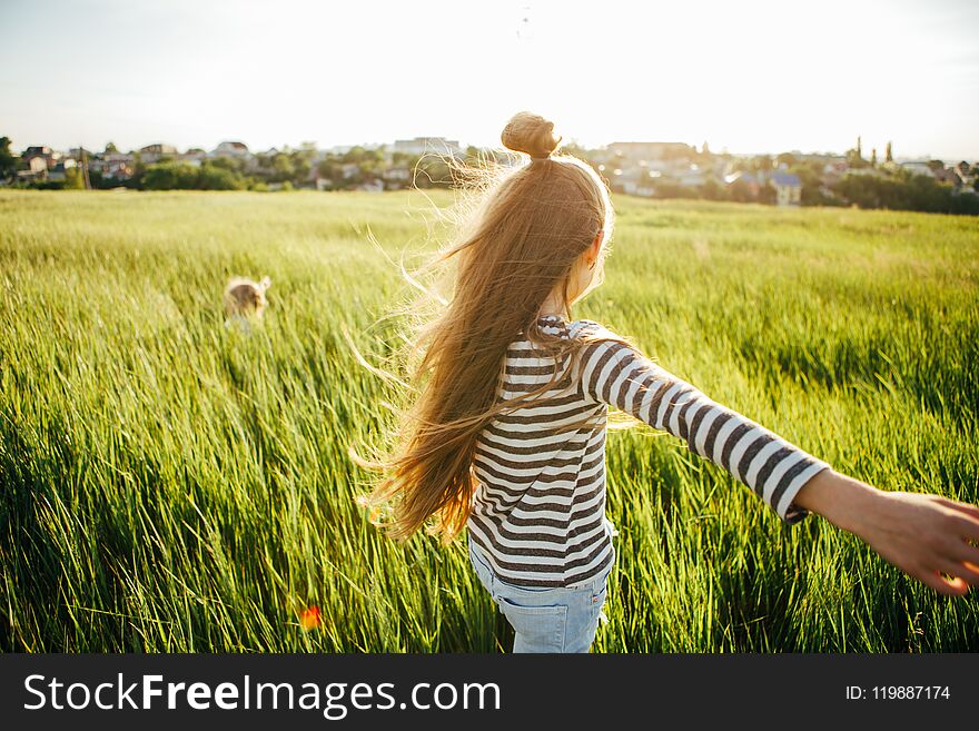 Children Playing Catch-up In The Green Field At Sunset.