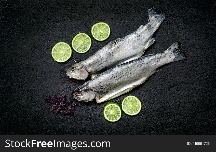 Two river trouts and ingredients on a black stone table