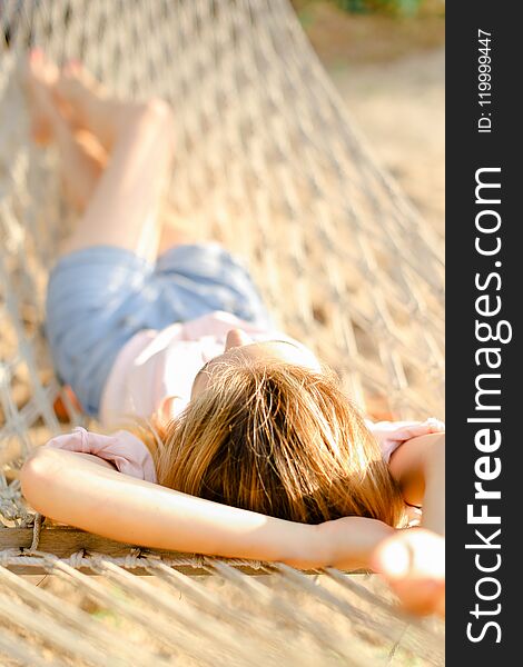 lose up young blonde girl lying in white wicker hammock, wearing jeans shorts and shirt. Concept of summer vacations and resting on beach. lose up young blonde girl lying in white wicker hammock, wearing jeans shorts and shirt. Concept of summer vacations and resting on beach.