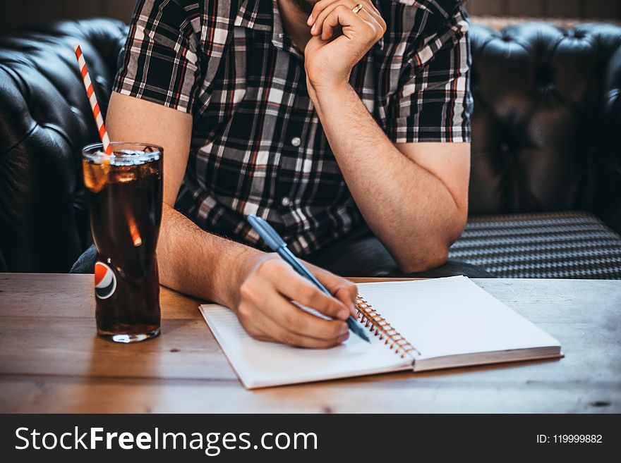 Man Holding Blue Pen Writing on White Notepad