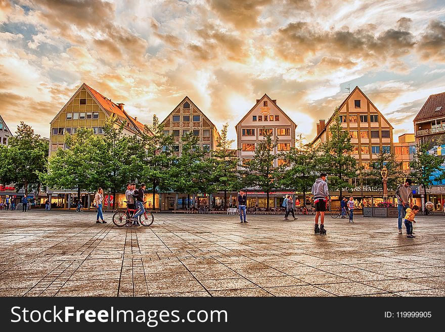 People On Concrete Pavement With Houses And Trees In Background