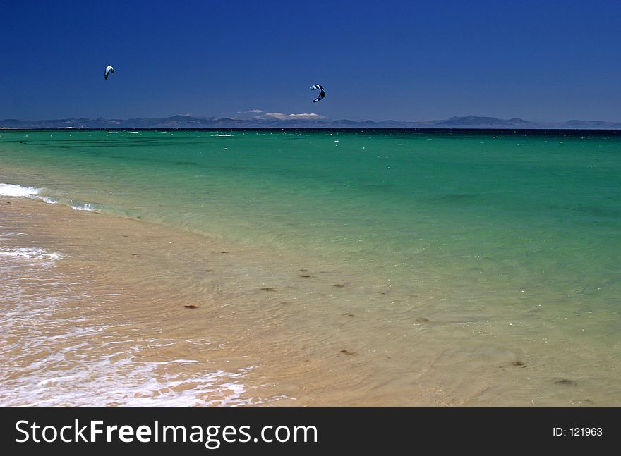View of kite surfers from a white sandy beach in Spain, Europe, on a hot sunny day on vacation.