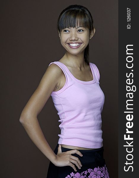 A pretty young asian woman in a pink top and black skirt with brown background. A pretty young asian woman in a pink top and black skirt with brown background