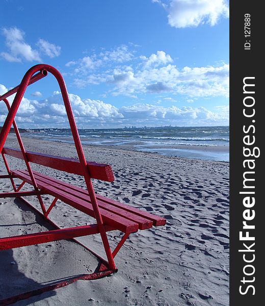 Red bench on the beach in windy summer day