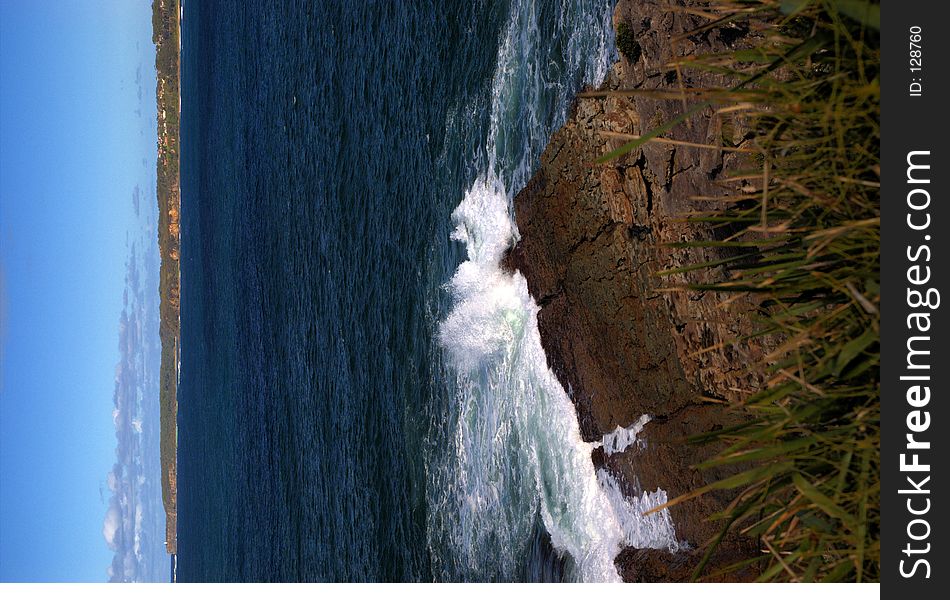 Waves crash against a rock shelf with a cliffline in the distance. Waves crash against a rock shelf with a cliffline in the distance