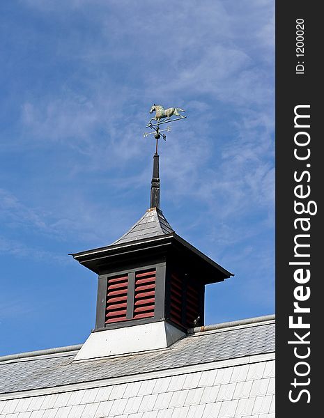 Copper horse weathervane on a barn's cupola that has green patina.