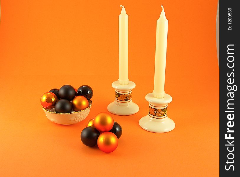 Bowl filled with orange and black balls, add candlesticks and candles all on an orange background. Bowl filled with orange and black balls, add candlesticks and candles all on an orange background.