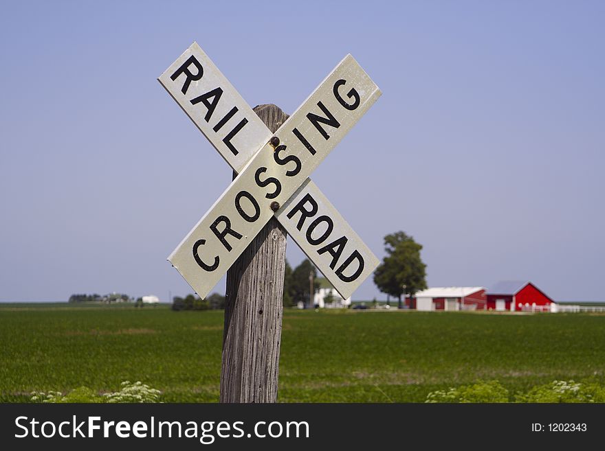 An old-fashioned railroad crossing sign with a farm scene in the background. An old-fashioned railroad crossing sign with a farm scene in the background