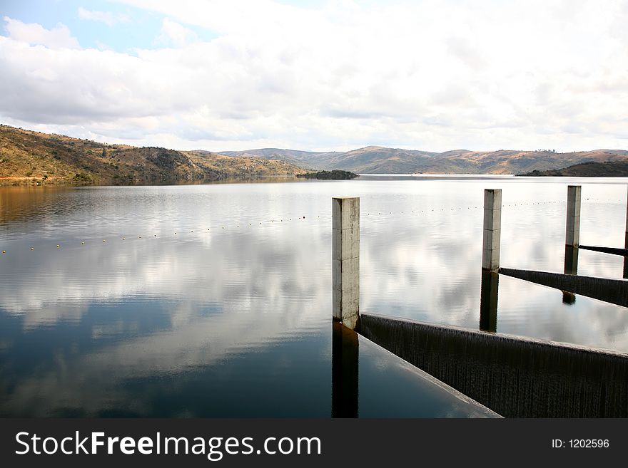 Dam wall and clouds reflecting on water. Dam wall and clouds reflecting on water