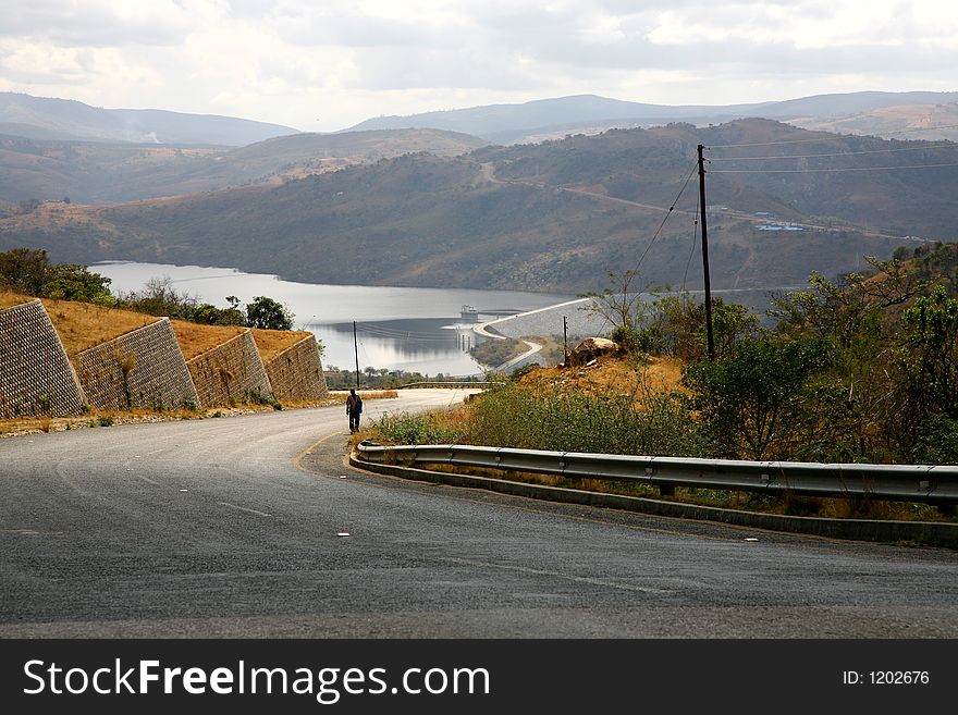 Curvy road leading to a lake with man walking in the road. Curvy road leading to a lake with man walking in the road.