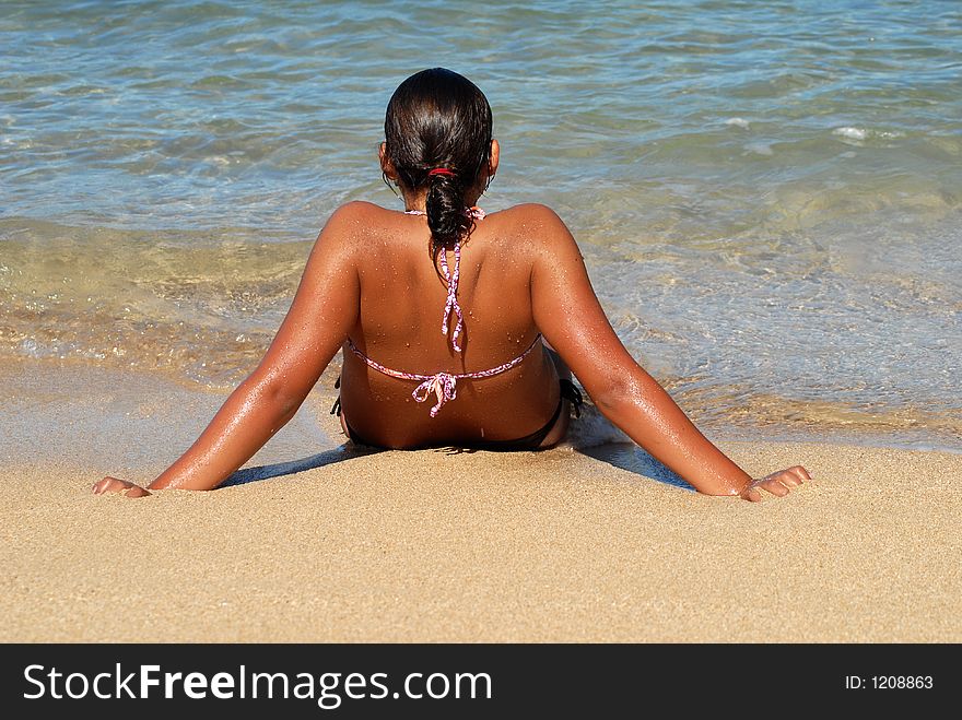 A teenager girl is sitting on the beach with feet in the water. A teenager girl is sitting on the beach with feet in the water