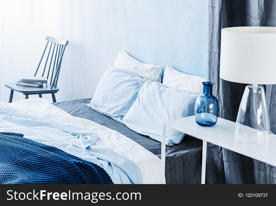White lamp on shelf in minimal blue bedroom interior with bed ne
