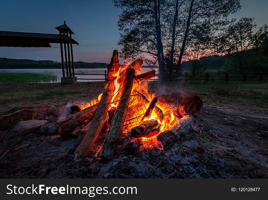 Calm bonfire at dusk by the lake in summer