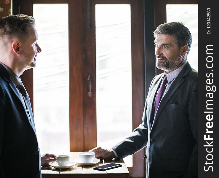 Two Person Talking in Front of Brown Wooden Table With Cup of Coffees