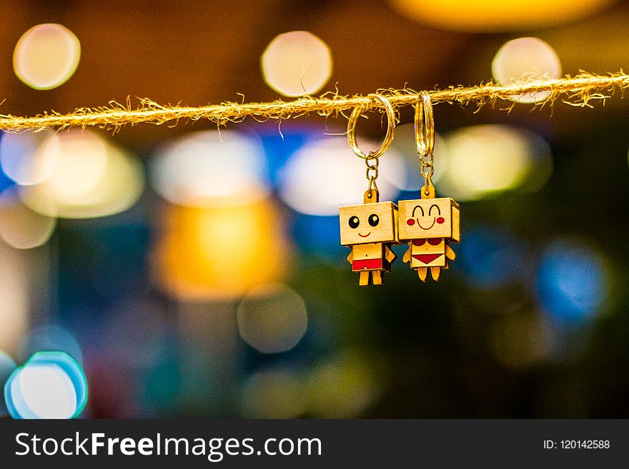 Two Man and Woman Wooden Couple Keychains Hanging on Rope Overlooking Bokeh Lights