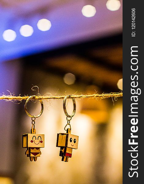 Bokeh Photography of Two Wood Block Man and Woman Figure Key Chains Hanging on Brown Thread