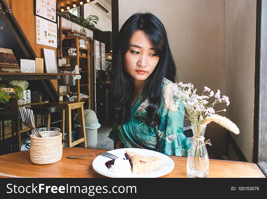 Beautiful Asian woman sitting in the cafe with a plate of dessert. Lifestyle concept.