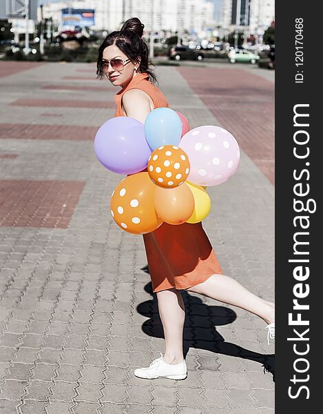 Happy young woman with balloons on the city square on a summer day