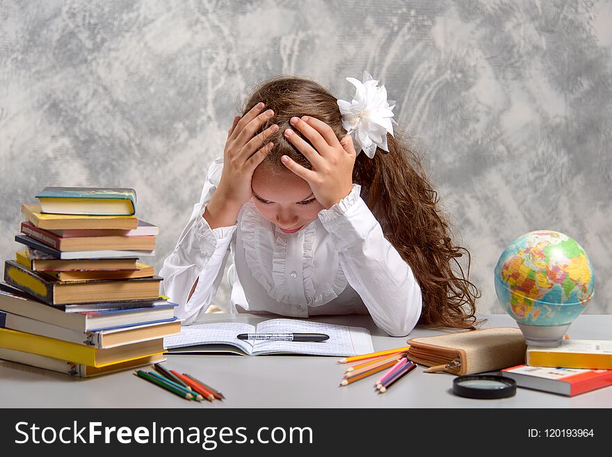 The schoolgirl in school uniform sits at the desk and thinks hard about the decision of the difficult task on a light gray background. Back to school. The new school year. Child education concept. The schoolgirl in school uniform sits at the desk and thinks hard about the decision of the difficult task on a light gray background. Back to school. The new school year. Child education concept.