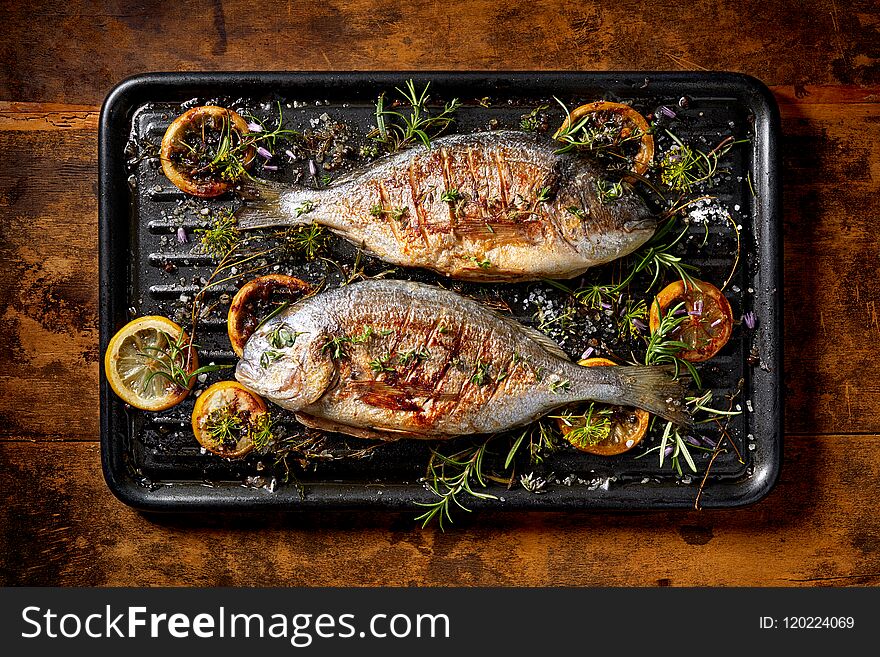 Grilled fish, sea bream, dorada with the addition of spices, herbs and lemon on the grill plate located on a wooden background