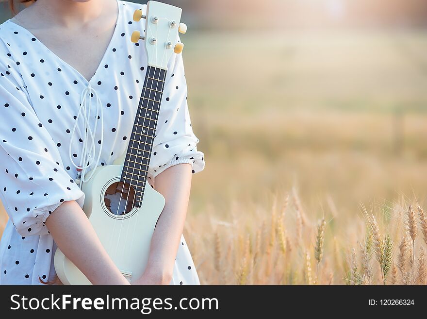 Beautiful asian woman playing ukulele and relaxing at barley field in summer on sunset time