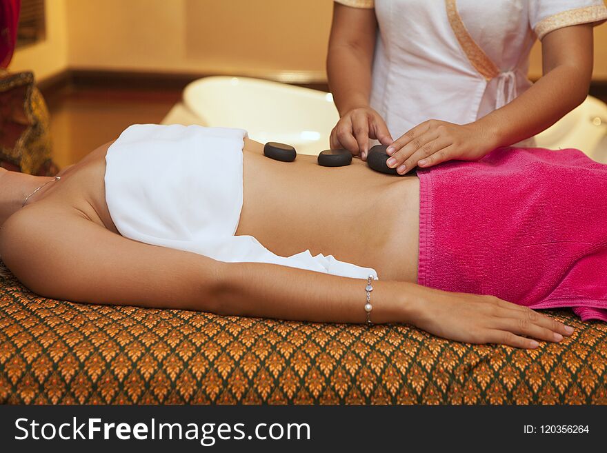 Beautiful woman having hot stones on her belly in spa salon.