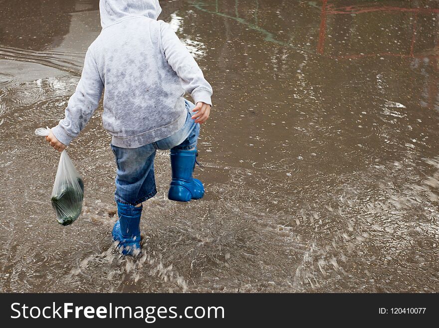 Little boy running around the puddles.