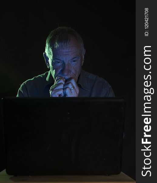 Serious senior man looking at a computer screen at night