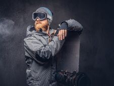 Brutal Redhead Snowboarder With A Full Beard In A Winter Hat And Protective Glasses Dressed In A Snowboarding Coat Royalty Free Stock Photo
