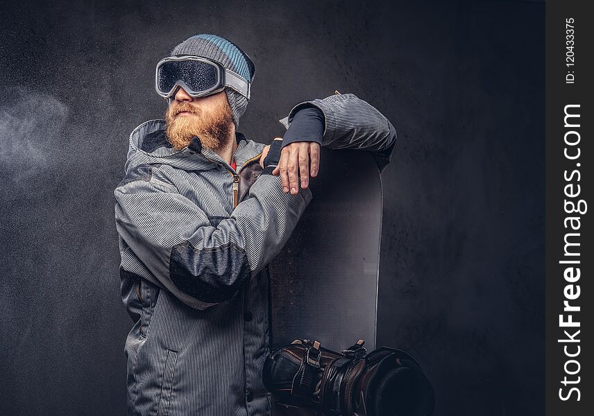 Brutal redhead snowboarder with a full beard in a winter hat and protective glasses dressed in a snowboarding coat
