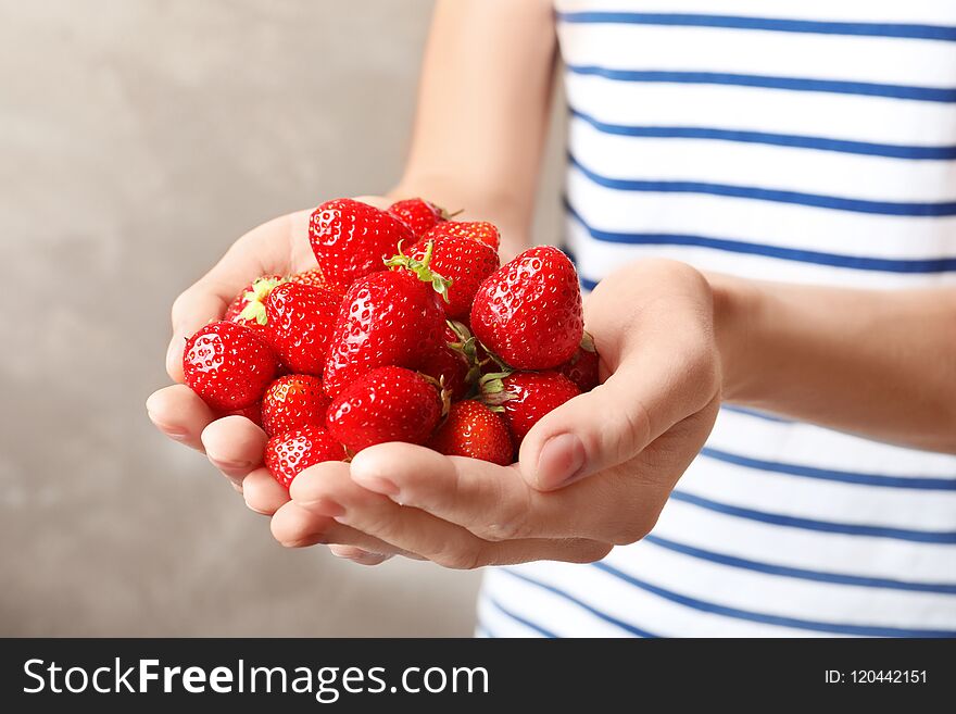 Woman holding ripe strawberries on grey background