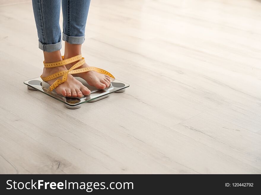Woman with tape measuring her weight using scales on wooden floor. Healthy diet