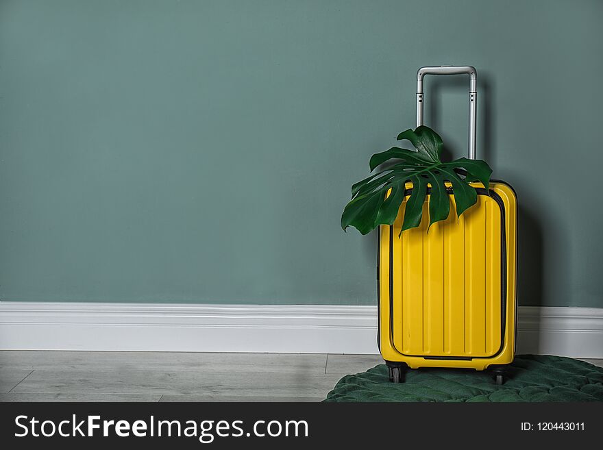 Bright yellow suitcase with tropical leaf near color wall indoors