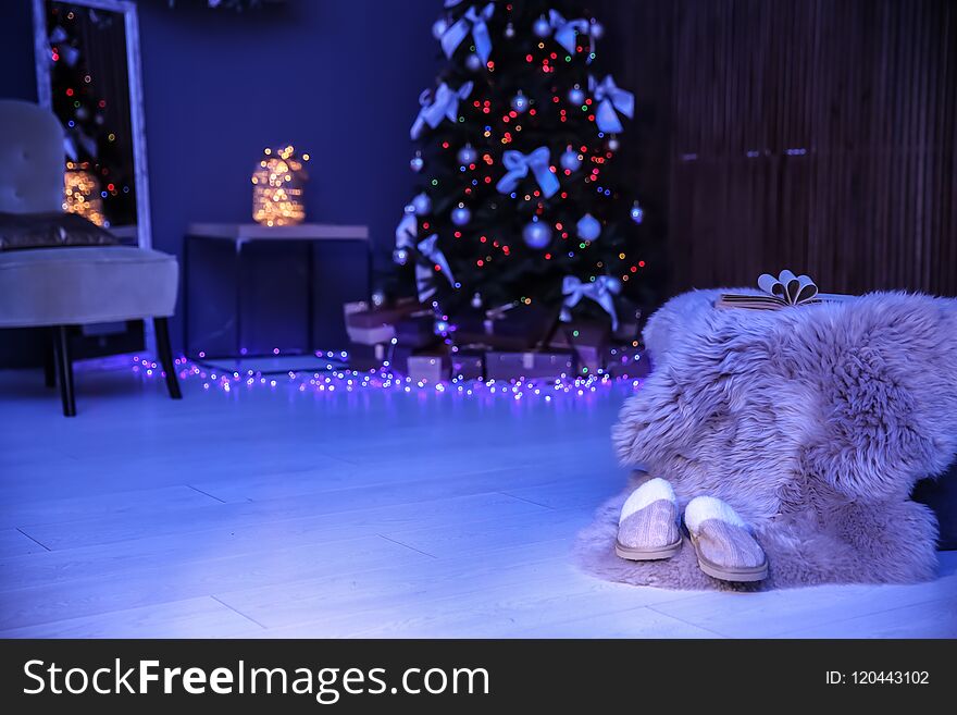 Soft slippers with fluffy blanket and Christmas tree in dark room