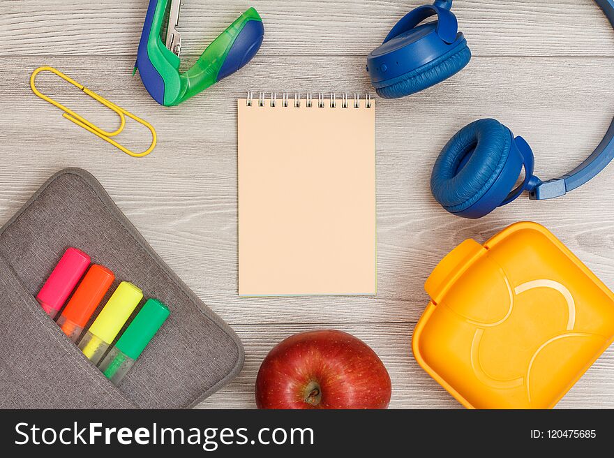 Bag-pencil case with color felt pens and marker, apple, pink notebook, stapler, headphones and lunch box on grey wooden background. Top view with copy space. Back to school concept. School supplies. Bag-pencil case with color felt pens and marker, apple, pink notebook, stapler, headphones and lunch box on grey wooden background. Top view with copy space. Back to school concept. School supplies.