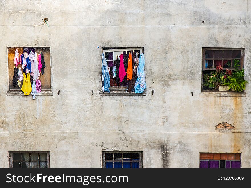 Square windows of homes with clothes and flowers in a decayed building with cracked walls. No people. Square windows of homes with clothes and flowers in a decayed building with cracked walls. No people.