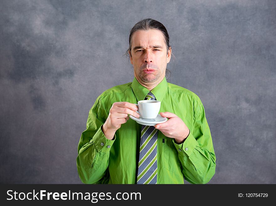 Young man in green shirt and necktie drinking not delicious coffee. Young man in green shirt and necktie drinking not delicious coffee