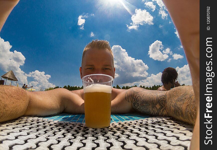 Beautiful young man enjoying beer at the pool outside