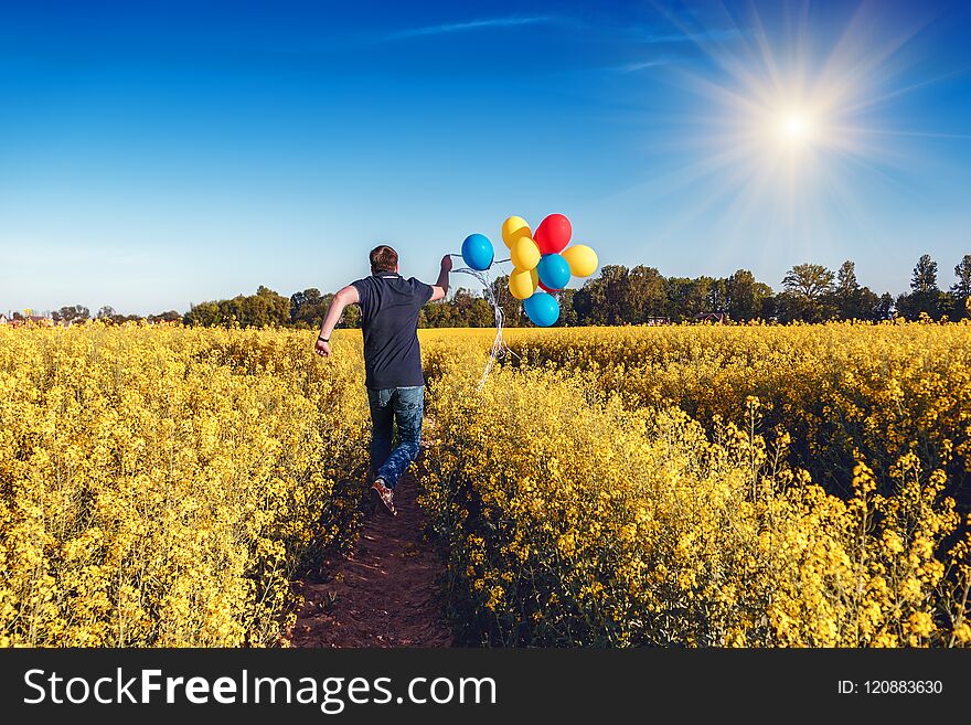 Jumping man with colored balloons in blooming field