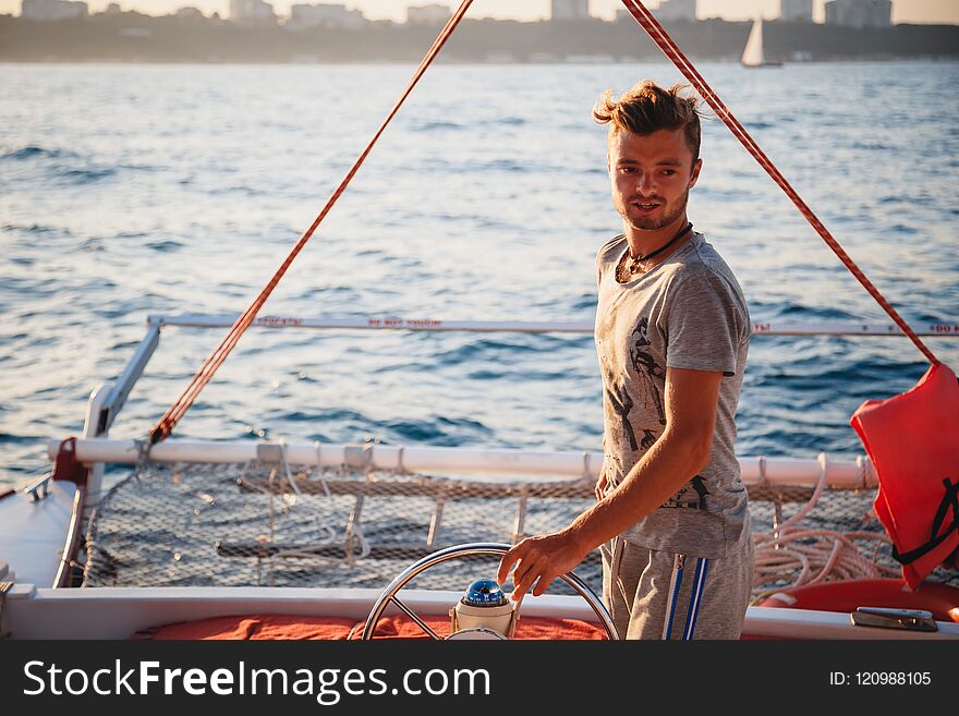 Young handsome man, captain driving yacht in sea at sunny day