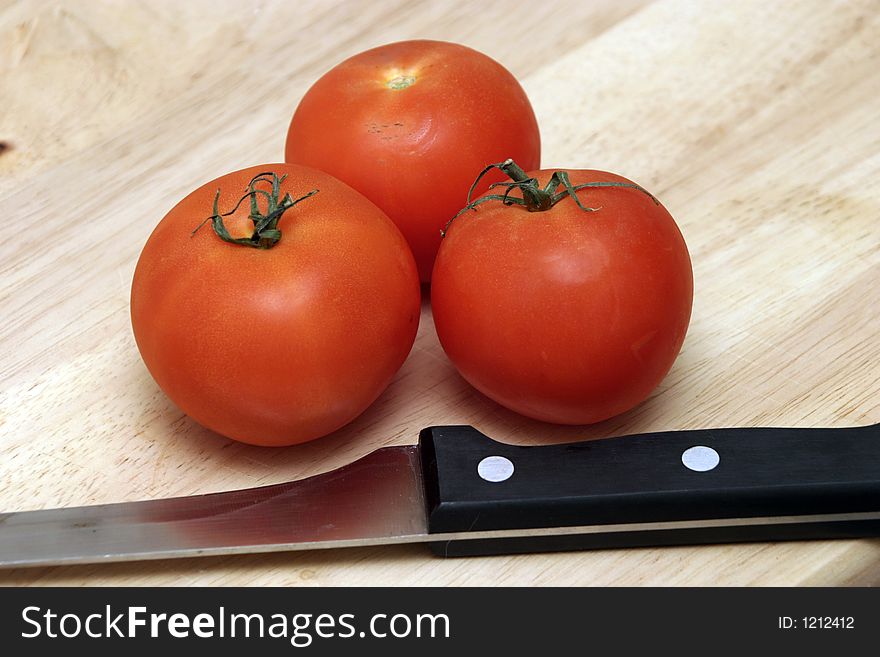 Three red tomatoes and a knife on a wooden chopping. Three red tomatoes and a knife on a wooden chopping