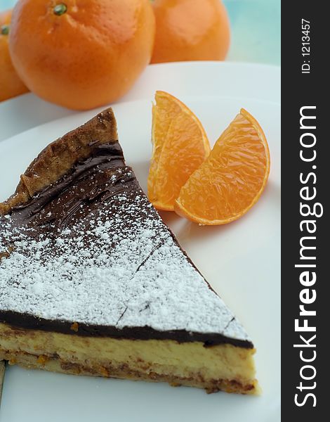 An angle view of a slice of chocolate mocha and orange cheesecake. Table setting with mandarin oranges for styling. Hue adjusted. An angle view of a slice of chocolate mocha and orange cheesecake. Table setting with mandarin oranges for styling. Hue adjusted.